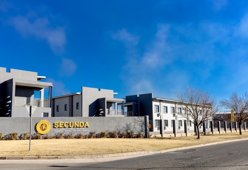 Modern hotel exterior with gray buildings, balconies, and signage for Secunda by Khayalami Hotel Group under a clear blue sky