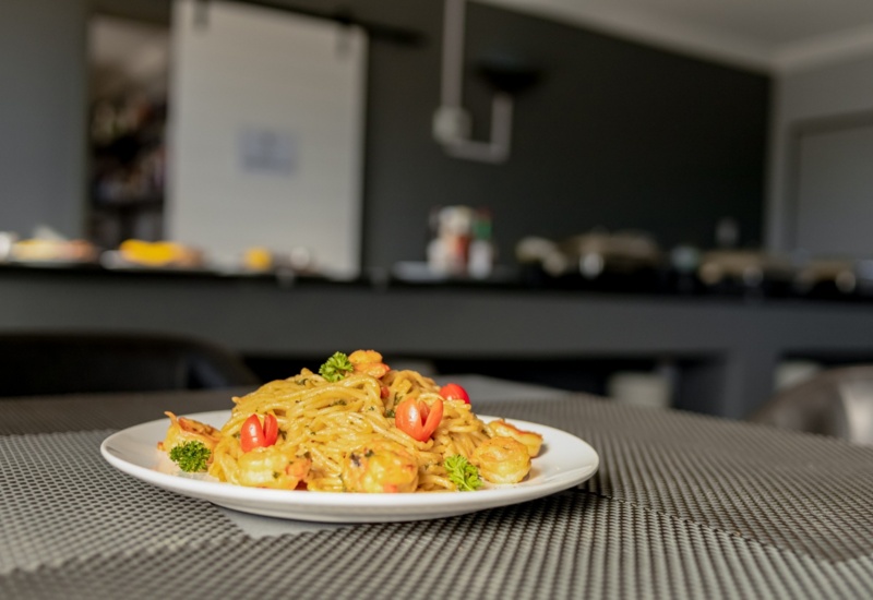 Plate of shrimp pasta garnished with parsley and cherry tomatoes on a gray mesh table in a modern dining area