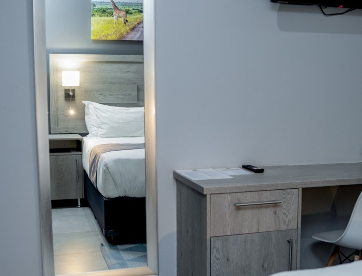 Modern hotel room with a neatly made bed reflected in a full-length mirror, featuring soft lighting and minimalist decor.