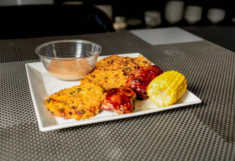 Crispy corn fritters with barbecue-glazed ribs, corn on the cob, and a creamy dipping sauce on a white plate