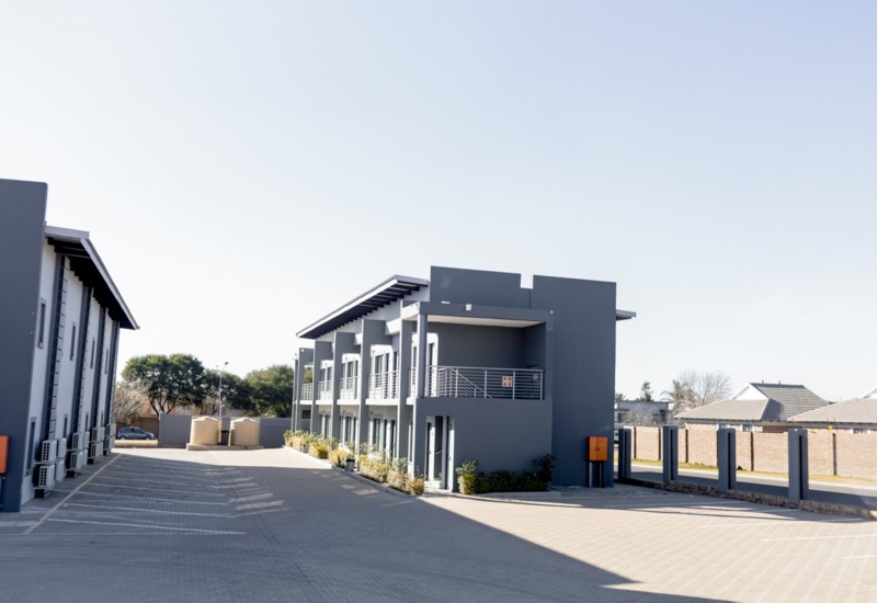 Modern two-story hotel building with gray exterior, private balconies, air conditioning units, and ample paved parking area