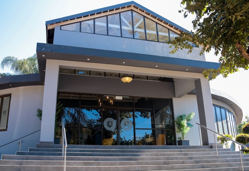Modern hotel entrance with large glass doors, high windows, wide staircase, and potted plants under a clear blue sky