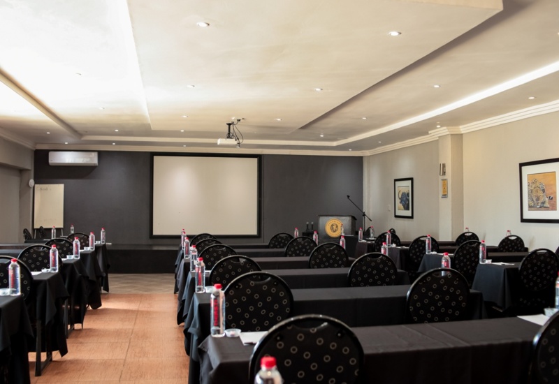 Modern conference room with black tablecloths, circular patterned chairs, bottled water, projector screen, and podium with microphone