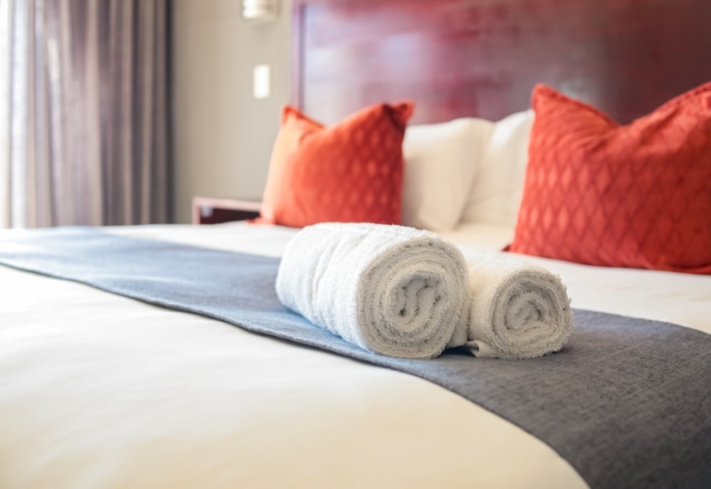 Hotel bed with crisp white linens, folded white towels on a blue runner, and vibrant orange accent pillows