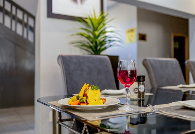 Modern dining table set with gourmet meal of vegetables and a creamy sauce, paired with a glass of red wine in elegant setting