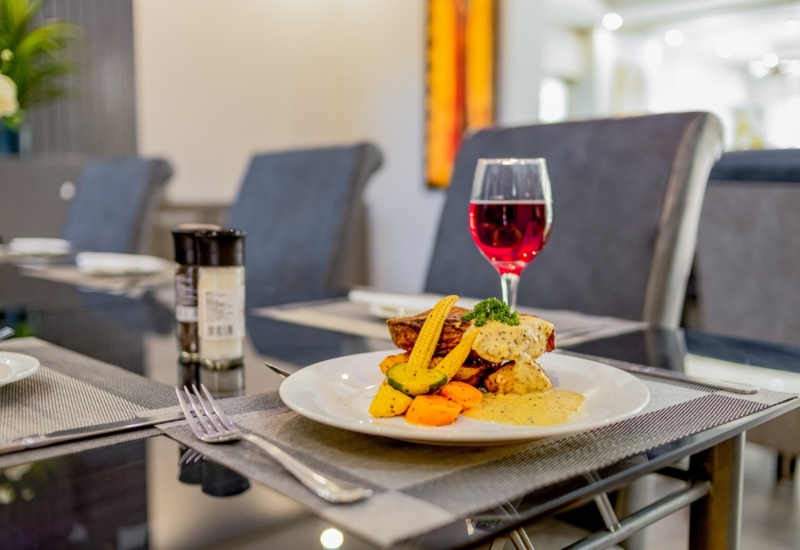 Grilled steak with creamy sauce, roasted vegetables, and a glass of red wine on a sleek dining table in a modern hotel restaurant