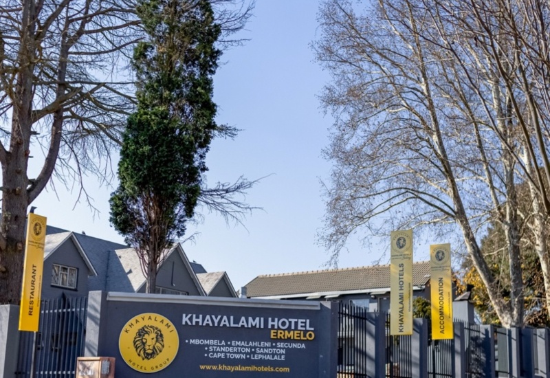 Exterior view of Khayalami Hotel Ermelo with clear signage, tall trees, and a calm, sunny atmosphere inviting guests.