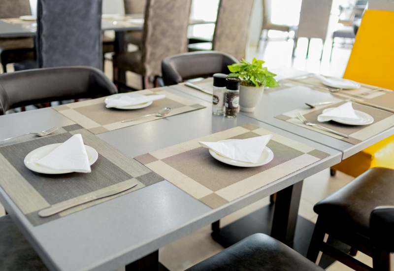 Modern hotel dining table set with neutral placemats, white folded napkins, black chairs, salt and pepper shakers, and a small potted plant