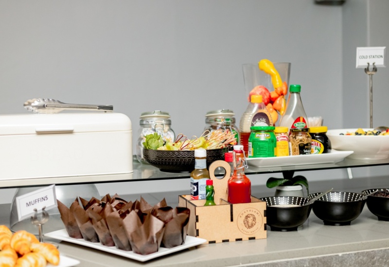 Breakfast buffet with muffins, croissants, fresh fruit skewers, condiments, jams, and salad dressings on a clean counter