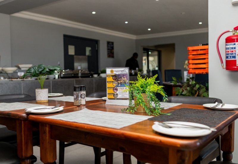 Cozy dining table set with plates, cutlery, salt and pepper shakers, and decorative plants in a modern hotel restaurant.