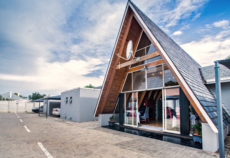 Modern A-frame guesthouse with large glass sliding doors, wooden interior accents, and covered parking spaces on a paved lot