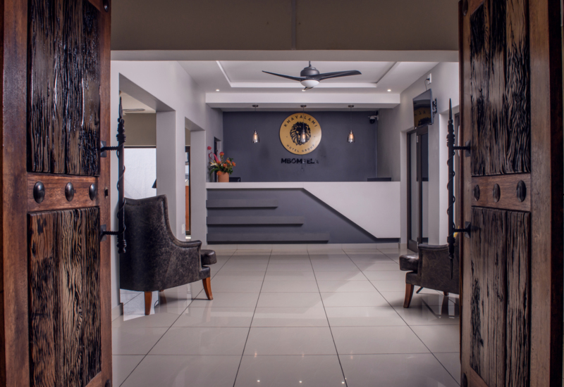 Reception area with a modern white desk, gray accent wall, pendant lights, dark armchairs, and rustic wooden doors open