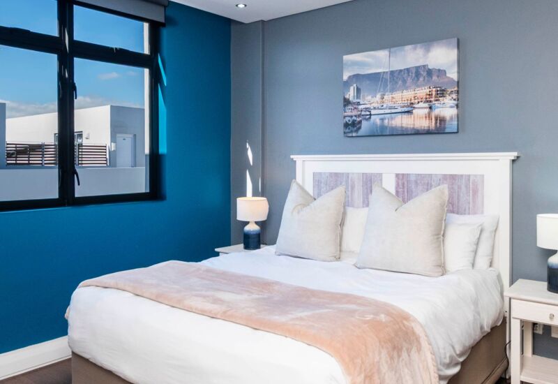 Cozy hotel bedroom with queen bed, soft beige and white linens, modern nightstands, blue accent wall, and cityscape wall art