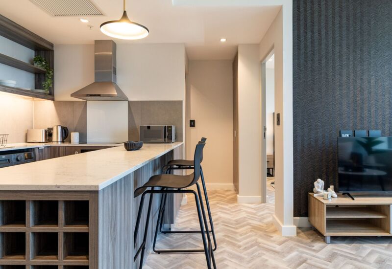 Modern kitchen and living area with marble countertop island, black bar stools, stainless steel appliances, and textured dark accent wall