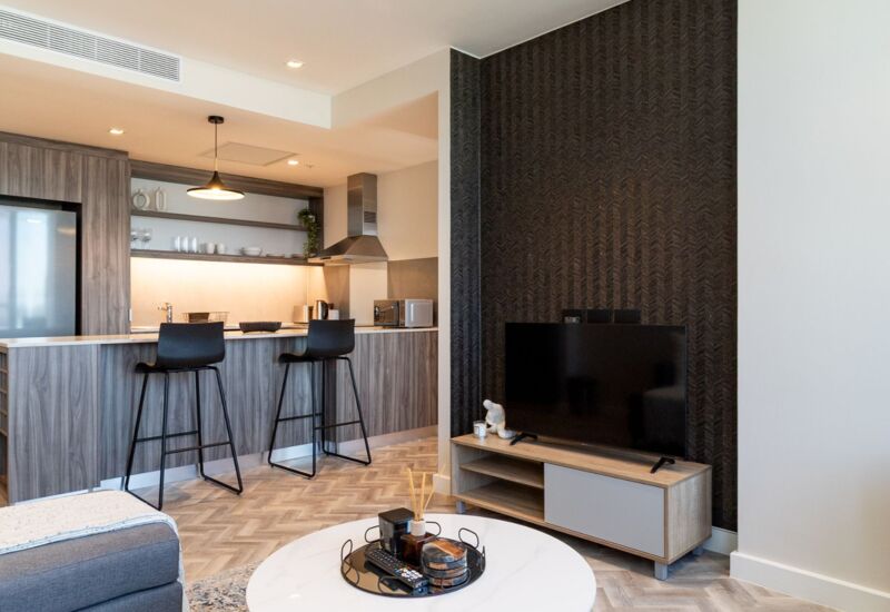Modern suite living area with open kitchen, breakfast bar with two stools, stylish TV console, and cozy seating area