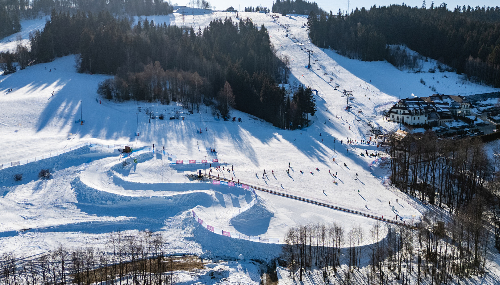 Ski resort with chair lifts, snowy slopes, guests skiing, and a lodge surrounded by forest on a sunny winter day.