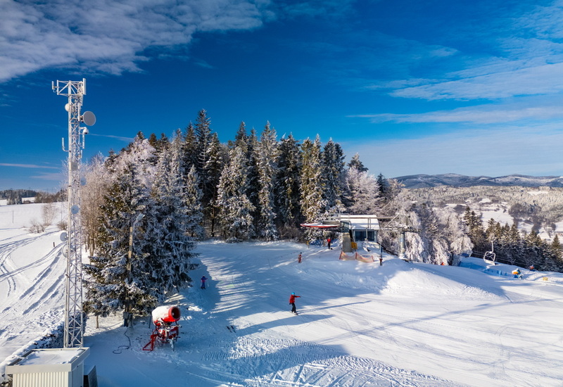 Snow-covered ski slope with chairlift, frosted trees, and skiers under a bright blue sky in a mountain resort.