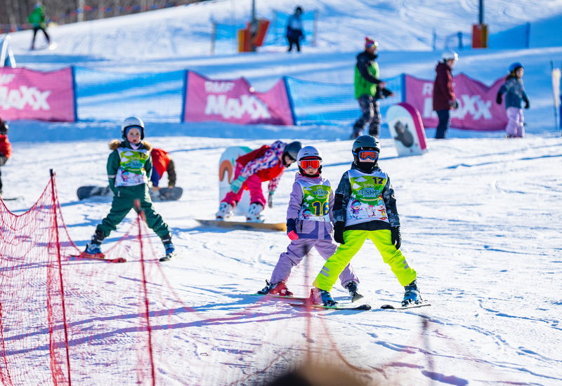 Children practicing skiing on a snowy slope at a ski resort, wearing colorful gear and helmets for safety.