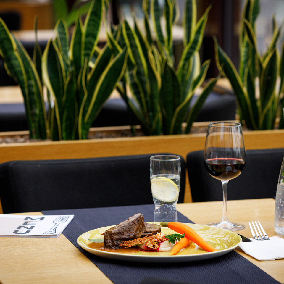 Wykwintne danie mięsne z marchewką, kieliszek czerwonego wina i woda z miętą na stoliku restauracyjnym z roślinami.