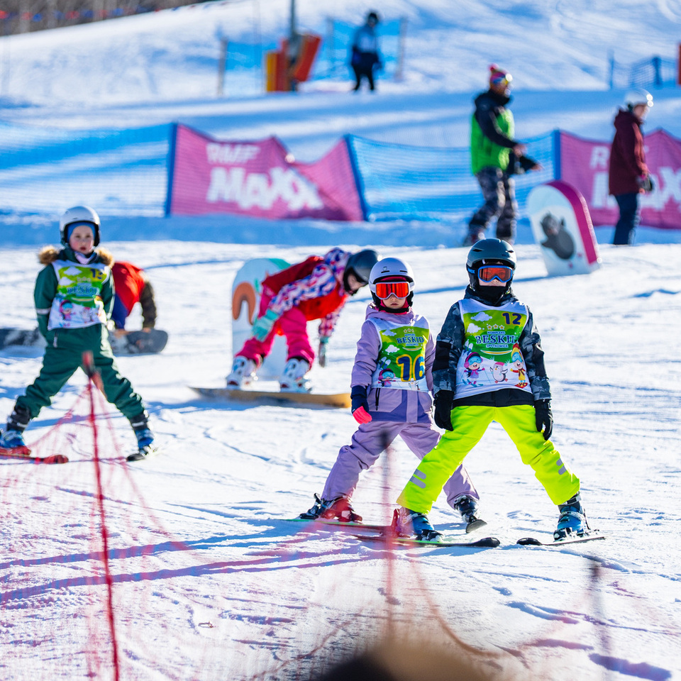 Dzieci uczą się jazdy na nartach w ośrodku narciarskim na zaśnieżonym stoku pod nadzorem instruktorów.