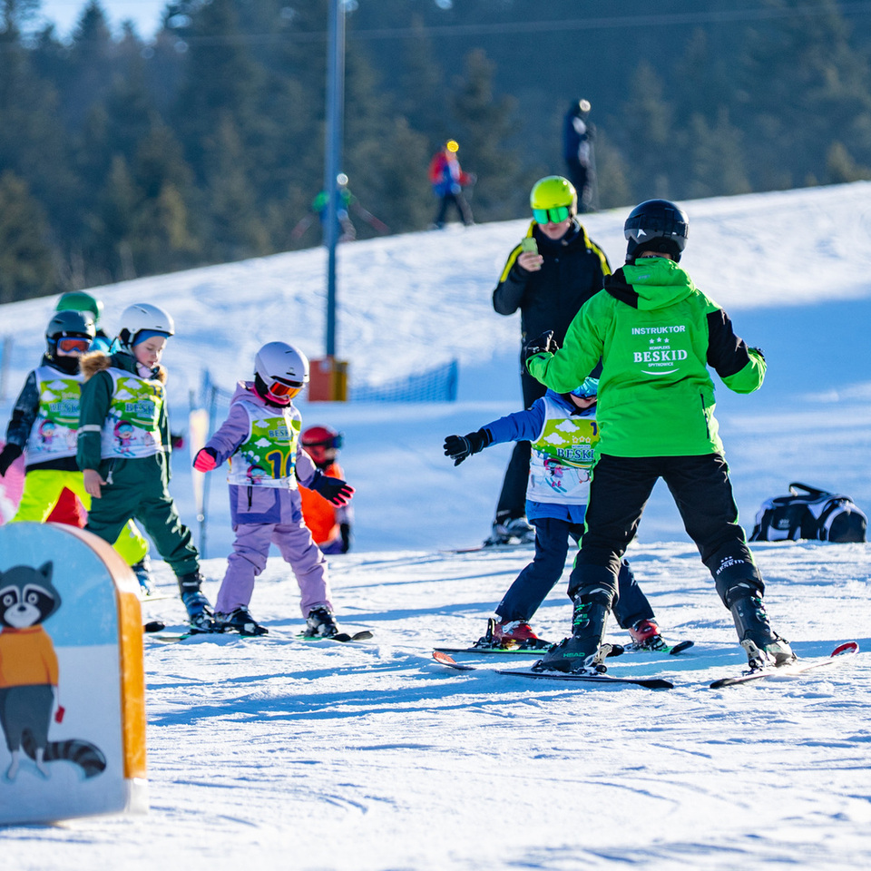 Instruktor uczy dzieci jazdy na nartach na ośnieżonym stoku z leśnym tłem podczas słonecznego dnia