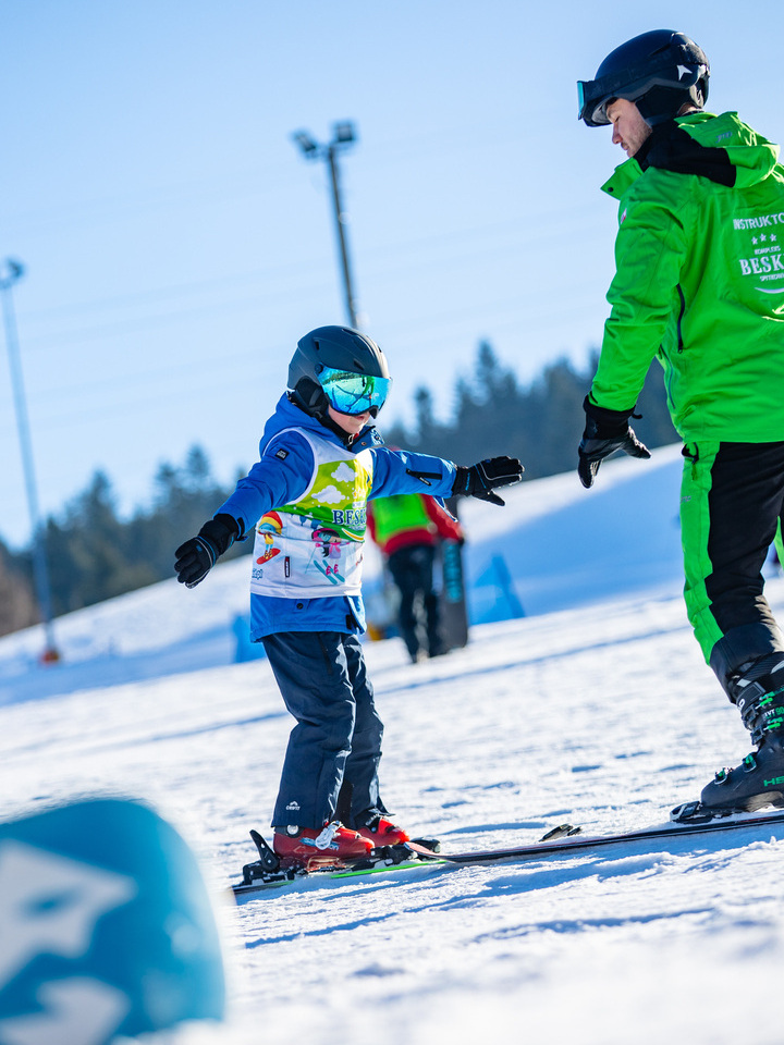 Ski instructor teaching a child how to ski on a snowy slope under clear blue sky