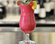 鲜艳粉色冰沙鸡尾酒，饰以薄荷、樱桃和柠檬皮，插吸管的高脚杯置于酒店吧台，背景瓶装饮品虚化