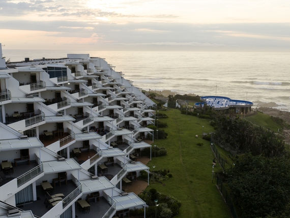 La Côte d’Azur with staggered private balconies, green lawn and circular blue-roof pool pavilion overlooking the sea.