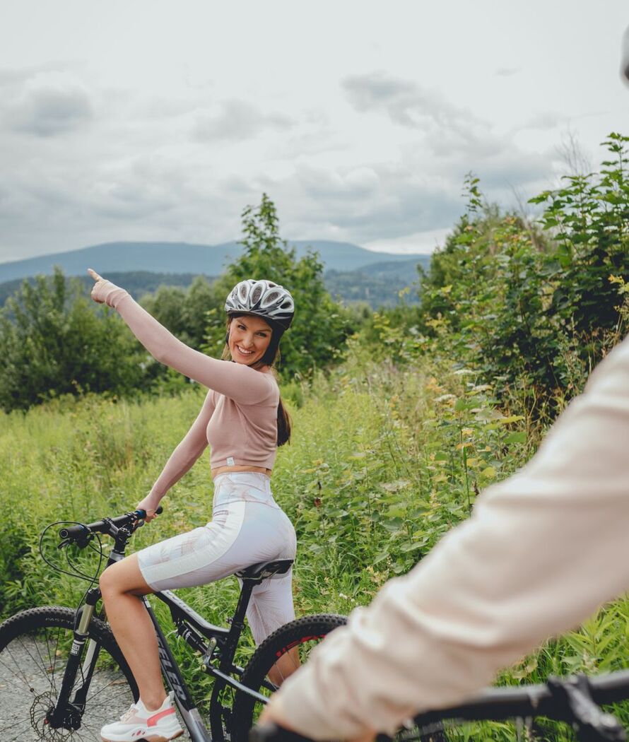 Urocza kobieta w kasku na górskim rowerze wskazuje na malownicze szczyty w tle podczas wycieczki rowerowej.