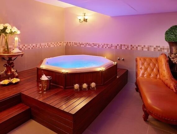 Private spa room with sunken wood-framed jacuzzi glowing blue, champagne on ice, lit candles, tufted leather sofa and soft ambient lighting