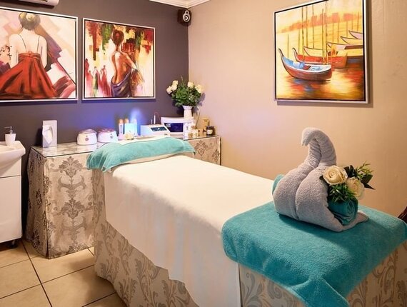 Tranquil spa room with massage table draped in teal towels, towel swan and roses, sink, treatment tools and colorful wall art