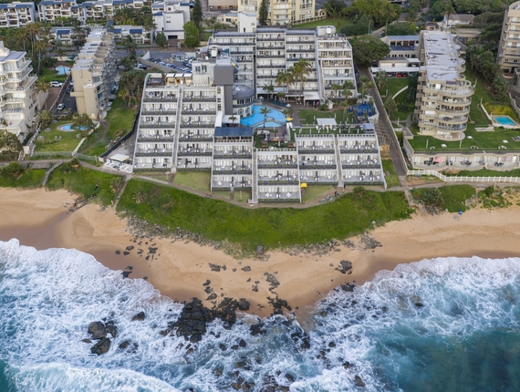 Oceanfront La Montagne with terraced rooms and private balconies, pool and palms, lawn with stairs to sandy beach and rocky shore.