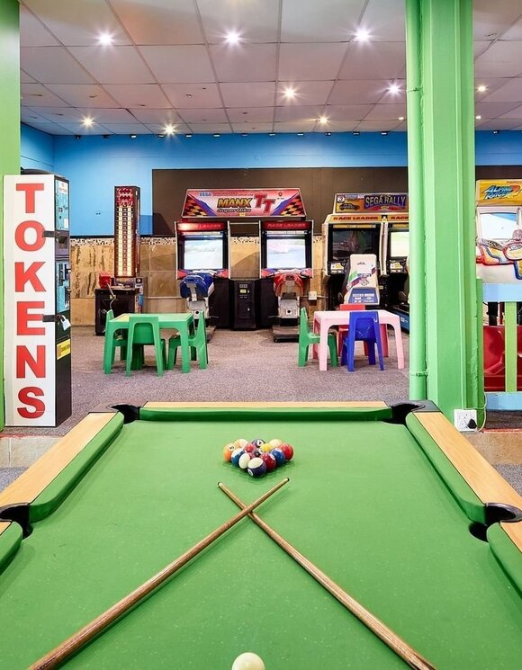 La Montagne Family game room with pool table and crossed cues, arcade racing machines, token dispenser and colorful kiddie tables