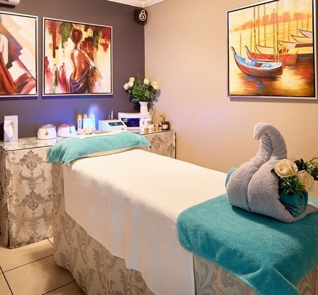 Tranquil spa room with massage table draped in teal towels, towel swan and roses, sink, treatment tools and colorful wall art