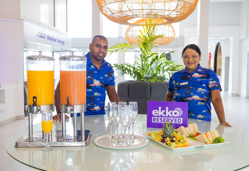 La Montagne hosts in tropical shirts behind lobby table with juice dispensers, glasses, fruit platter, sandwiches and 'ekko reserved' sign