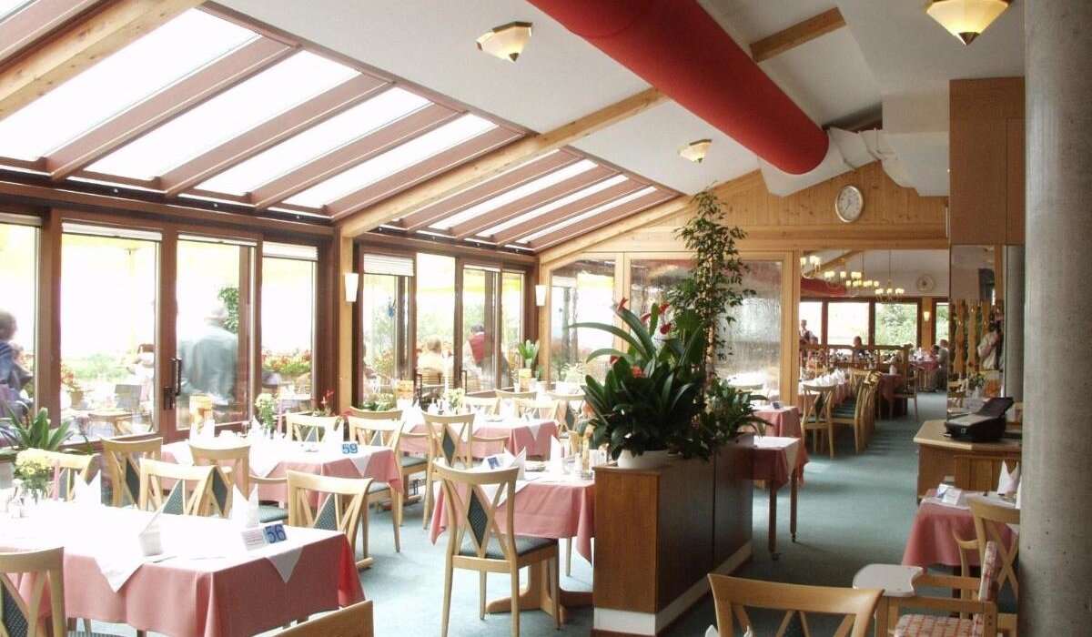 Helles Restaurant mit großen Panoramafenstern und Wintergarten-Atmosphäre, stilvoll gedeckter Tische