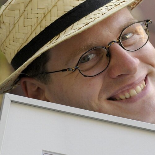 Hotelinhaber mit Strohhut und Brille lächelt freundlich in die Kamera