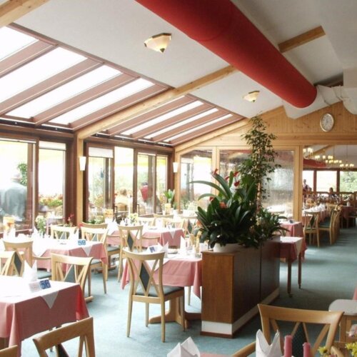 Helles Restaurant mit großen Panoramafenstern und Wintergarten-Atmosphäre, stilvoll gedeckter Tische