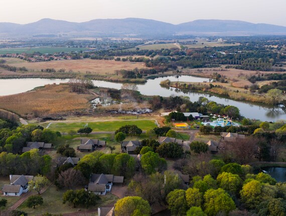 Lakeside resort with clustered cottages among trees, waterpark and pool, soccer field, winding lagoon and mountain views.