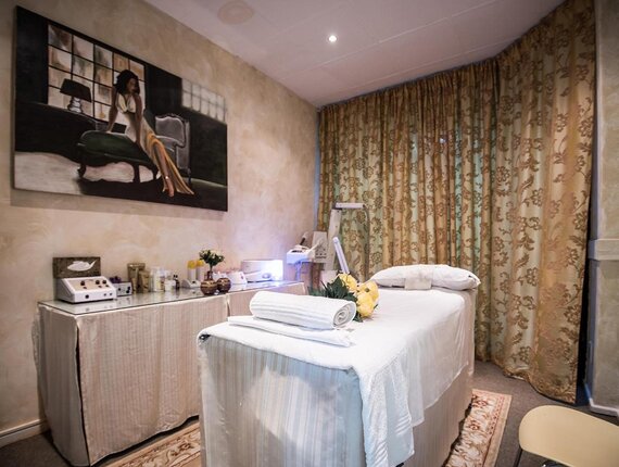 Spa treatment room with white-sheeted massage table, rolled towel and yellow flowers, skincare devices on side counter.