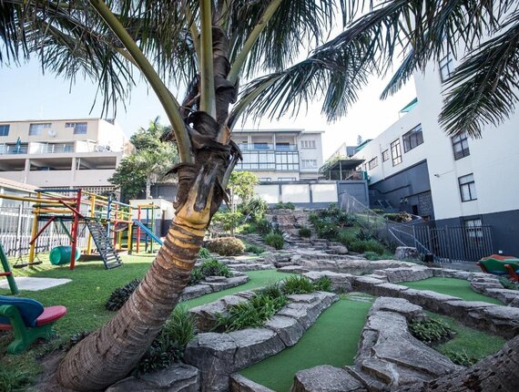 Palm-shaded courtyard with mini-golf carved into rock, colorful children's playground and outdoor seating by hotel buildings.