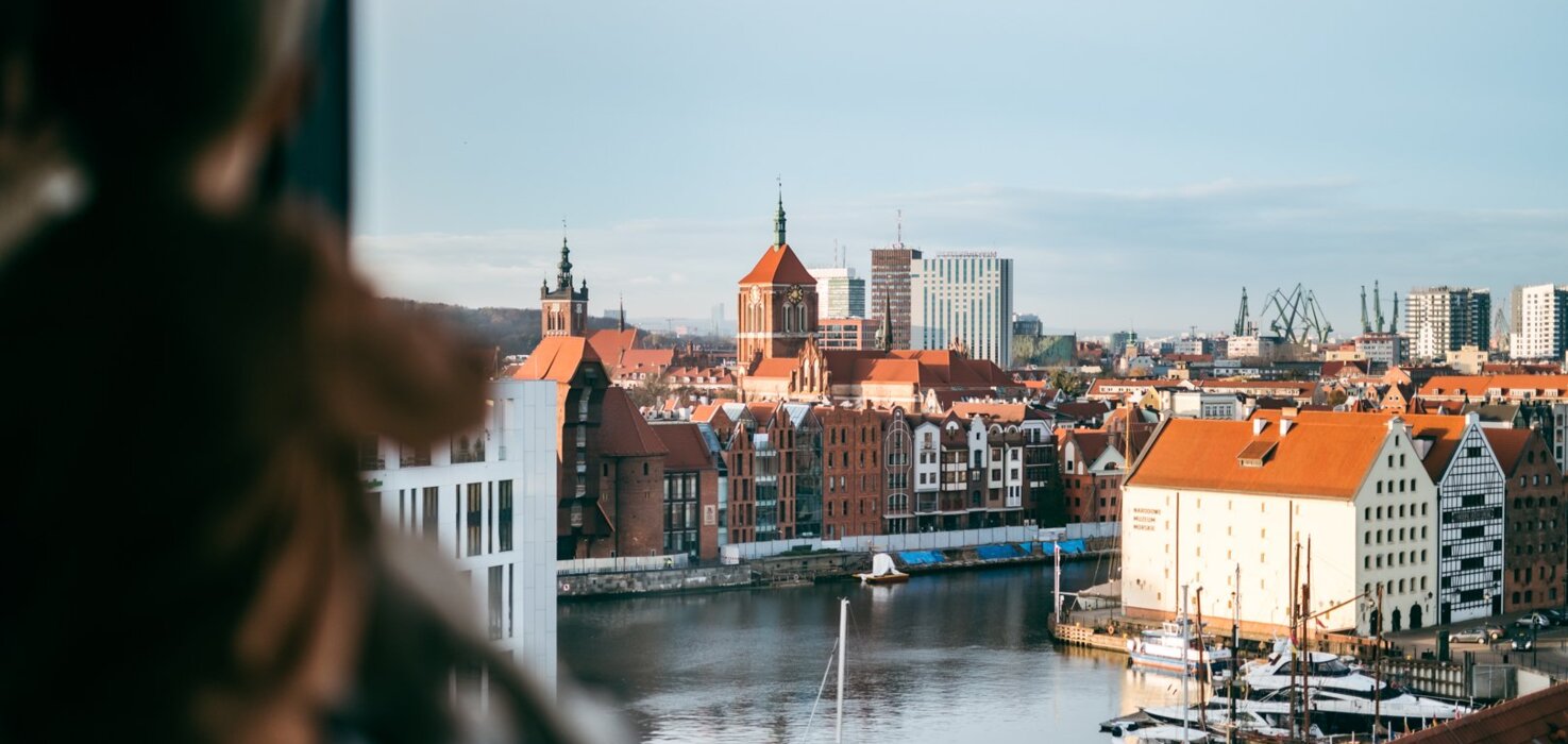 Výhled z hotelového pokoje na historický přístav s plachetnicemi, středověkými budovami a moderními kancelářskými budovami