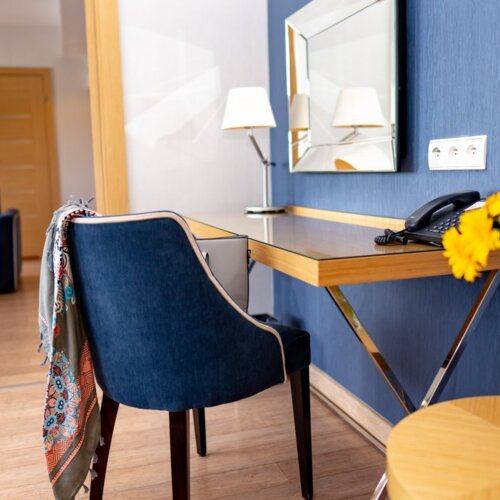 Apartament hotelowy z niebieskimi ścianami. Krzesło przy biurku z żółtymi kwiatami.