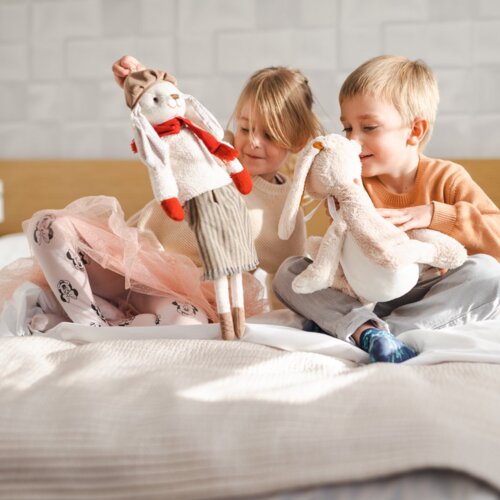 Chłopiec i dziewczynka radośnie bawią się pluszowymi królikami na łóżku.