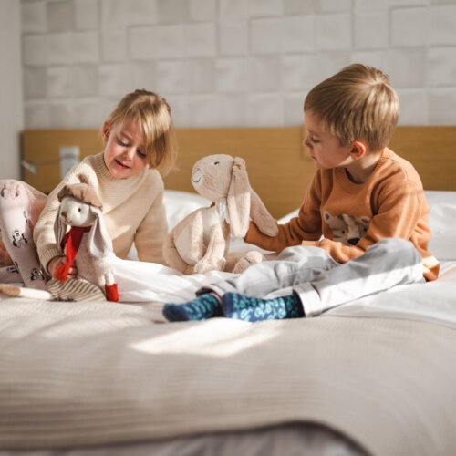 Chłopiec i dziewczynka radośnie bawią się pluszowymi królikami na łóżku.