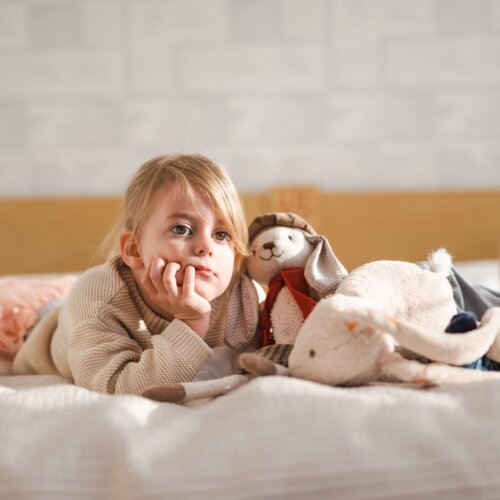 Zamyślona dziewczynka leży na łóżku z dwoma pluszowymi króliczkami.