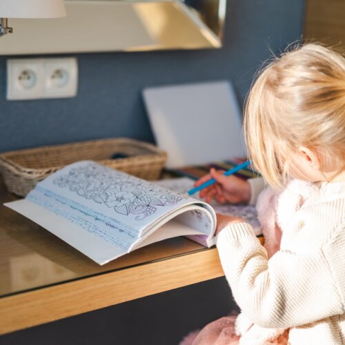 Dziewczynka siedząca przy biurku i kolorująca w książce z kolorowankami.