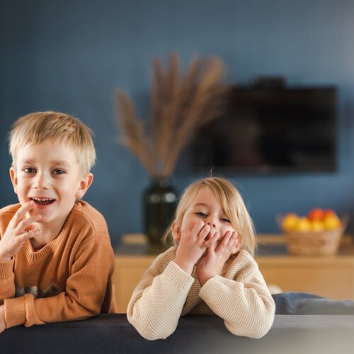 Dwoje uśmiechniętych dzieci opiera się o oparcie kanapy.