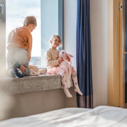 Chłopiec i dziewczynka trzymająca maskotkę różowego królika, którzy siedzą na parapecie okna.