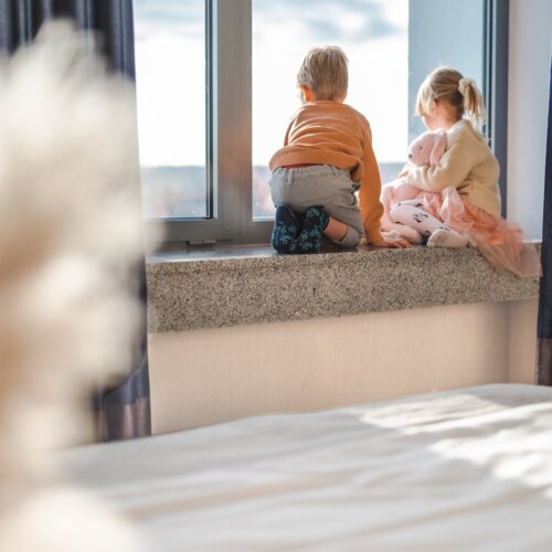 Chłopiec i dziewczynka z pluszowym, różowym królikiem siedzą na parapecie i patrzą przez okno.